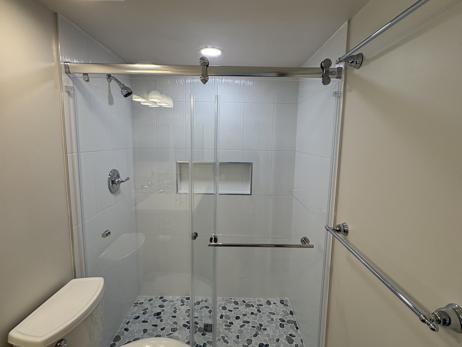 Finished walk-in shower with large-format tile, pebble floor, niche shelf and frameless sliding glass