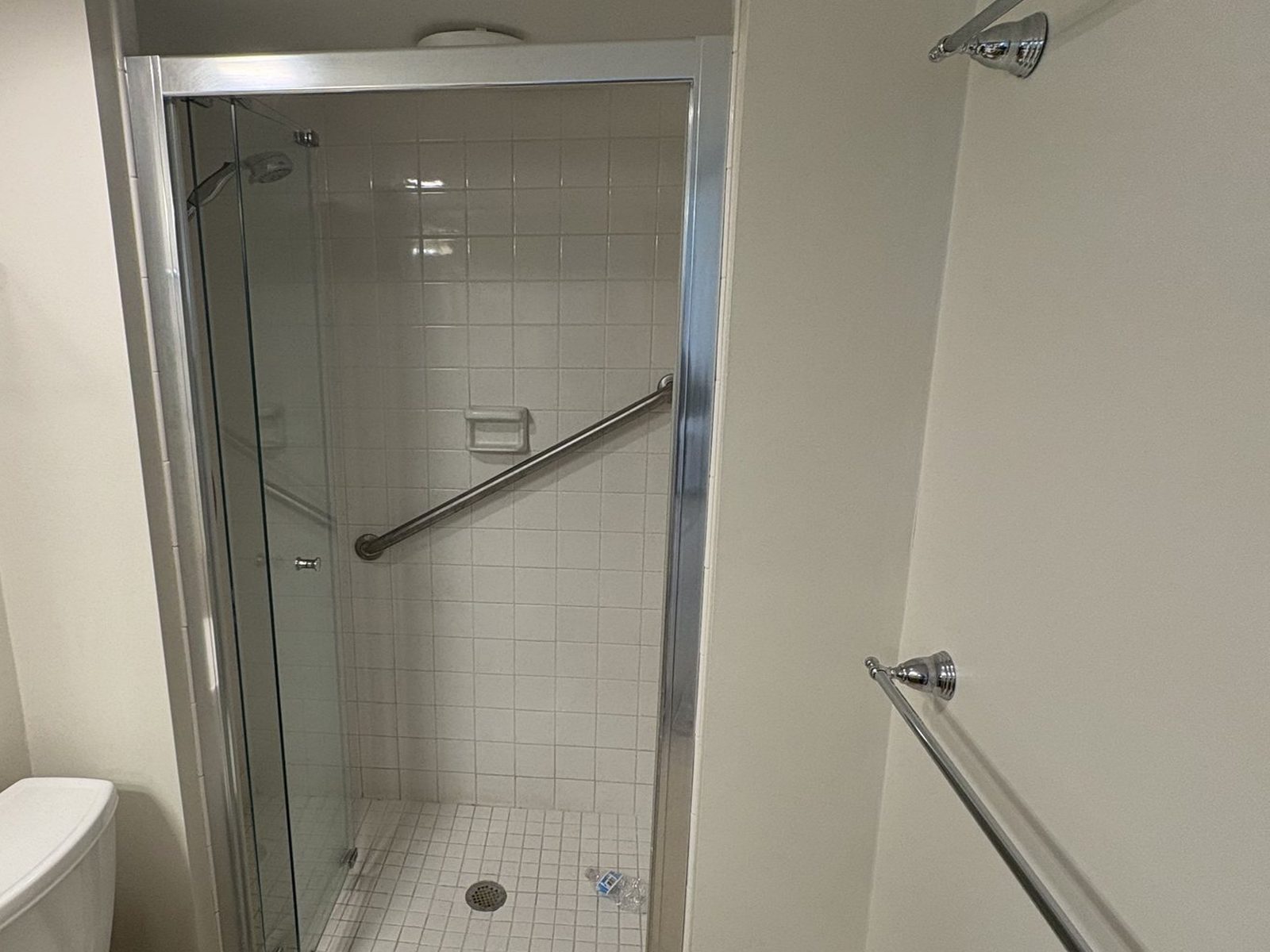 Dated walk-in shower with small white tile, framed glass door and grab bar — before NoBull Man