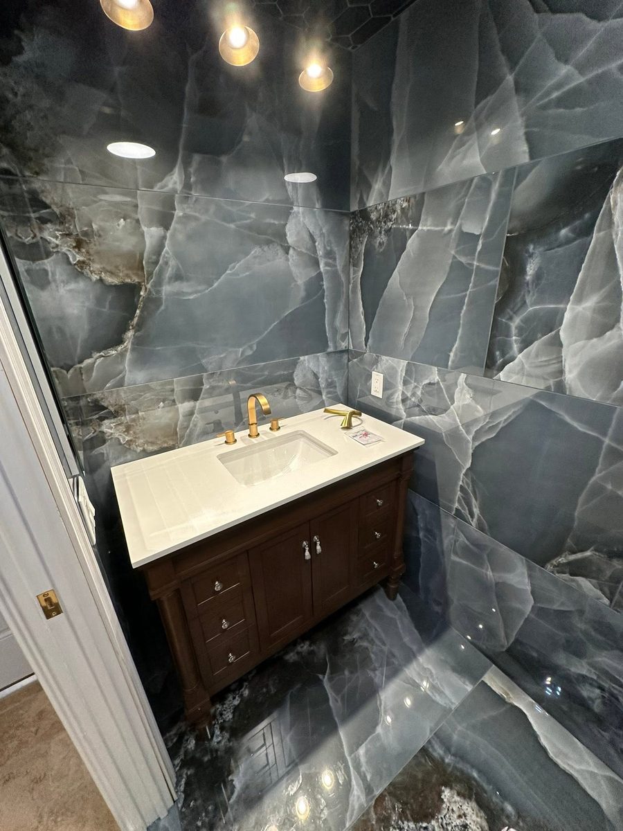 Dark marble bathroom with gold fixtures and wood vanity by No Bull Man
