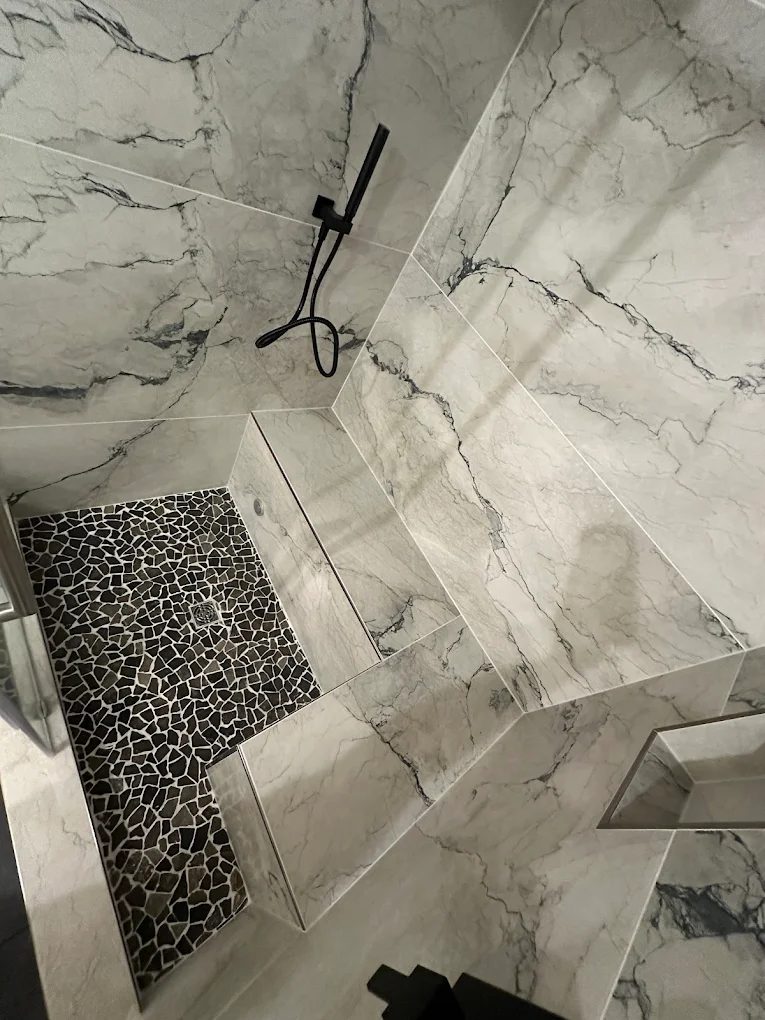 Custom marble walk-in shower with pebble floor and built-in bench by No Bull Man